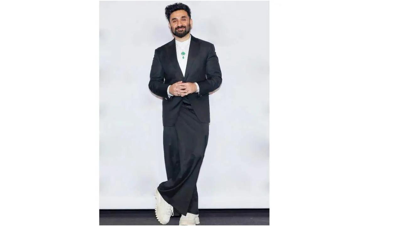 वीर दास, जिन्होंने अपने लुक को डिज़ाइन करने के लिए नई प्रतिभाओं की तलाश के लिए देश भर में अभियान चलाया था, ने 4,000 से ज़्यादा प्रविष्टियों में से दिल्ली की रहने वाली शुभांगी बाजपेयी को चुना. विजेता पोशाक एक सूट थी जिसमें एक क्रिस्प सिंगल-बटन टेलर्ड जैकेट और प्लीटेड लुंगी-प्रेरित पैंट (फाइन वूल सूटिंग में बनी) शामिल थी. दास ने एक आधुनिक कमरबंद पहना था, जिसमें बटन बंद था और एक मिनिमल एमरल्ड नेकलेस था. (तस्वीर में: इंटरनेशनल एमी अवार्ड्स में वीर दास. तस्वीरें सौजन्य/इंस्टाग्राम)