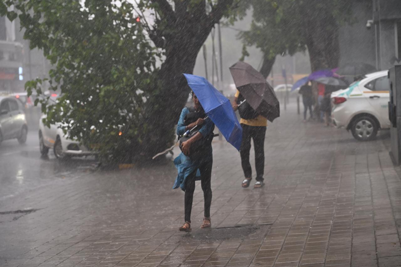 बारिश के साथ हवा चलने के कारण बौछार से बचते लोग.