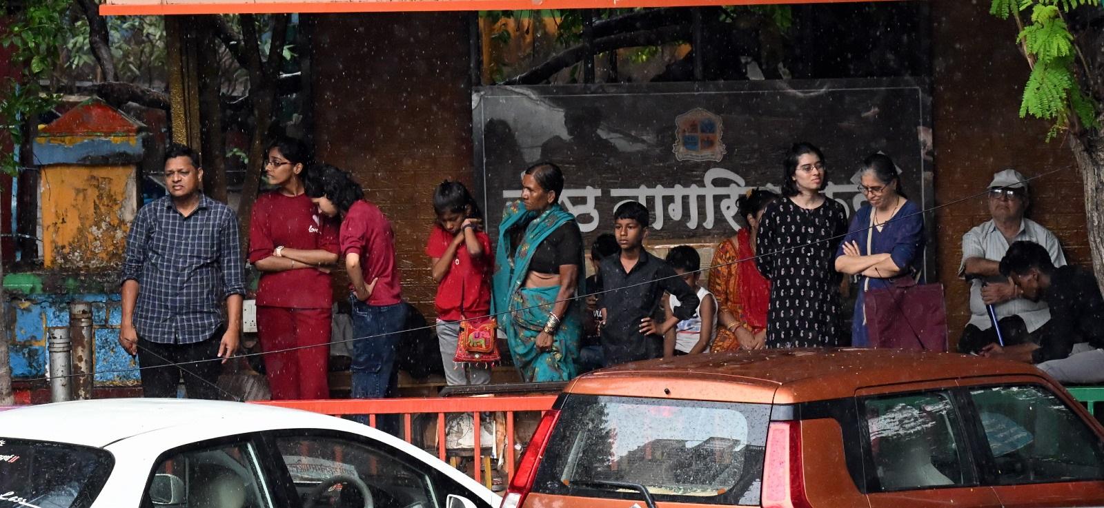 तेज बारिश के कारण लोग सड़क के किनारे बारिश रुकने का इंतज़ार कर रहे थे.