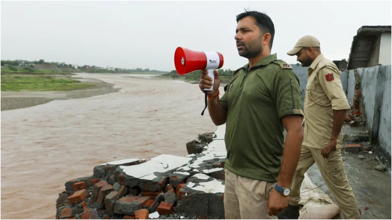 जम्मू में भारी बारिश के बाद तवी नदी के पास लोगों को चेतावनी देने और उन्हें सुरक्षित निकालने की तैयारी करते पुलिसकर्मी. तस्वीर/पीटीआई