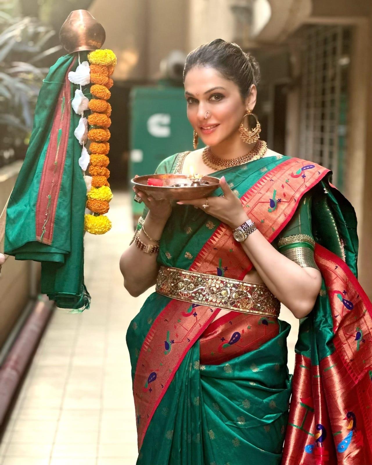 पारंपरिक हरे रंग की सिल्क साड़ी - क्लासिक एलिगेंस
यह हरी सिल्क साड़ी लाल बॉर्डर और कोरल पिंक टच के साथ पारंपरिक भारतीय सुंदरता की मिसाल है. गहरे हरे रंग की रेशमी साड़ी पर कोरल बॉर्डर का मोटिफ वर्क और उसकी बारीकी इसे खास बनाती है. ईशा ने इसे पारंपरिक और शानदार गोल्ड ज्वेलरी से सजाया है, जिसमें एक आकर्षक चोकर नेकलेस, बड़े हूप इयररिंग्स और कई चूड़ियाँ शामिल हैं, जो साड़ी के शाही आकर्षण को और बढ़ा देती हैं. उनके बालों को पीछे की ओर बाँधकर ताज़े फूलों से सजे एक साफ-सुथरे जूड़े में बाँधा गया है, और उनका मेकअप नेचुरल व सॉफ्ट – जिससे साड़ी की सुंदरता केंद्र में बनी रहती है.